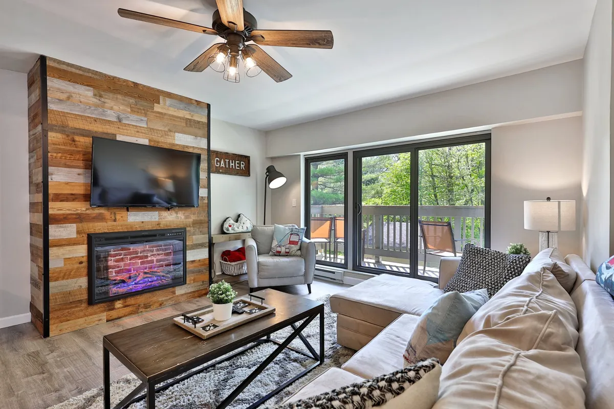 A cozy living area featuring a wood accent wall, electric fireplace, large windows, and plush seating. The inviting space is designed for relaxation, whether you're enjoying quiet moments by the fire or taking in views from the windows.