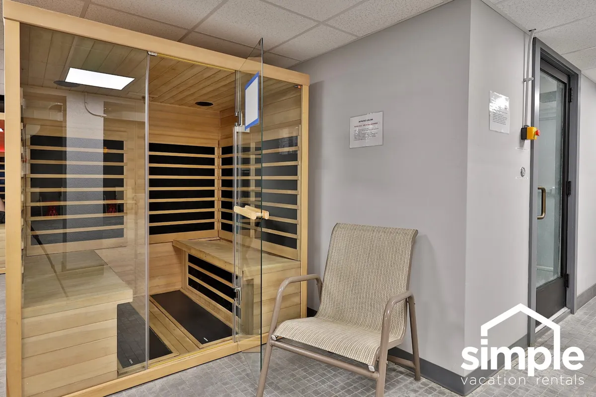 A tranquil interior space centered on a glass sauna and a wooden bench, with a woven chair adding a touch of cozy comfort. The setup evokes moments of peaceful heat therapy and introspection.