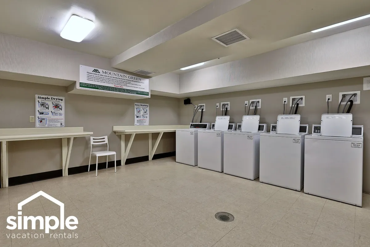 A practical laundry facility with multiple washing machines, a drying area, and a folding table. Informational signage on the wall indicates a communal aspect, and the overall setting is clean and functional—ideal for keeping adventure gear and clothing fresh.