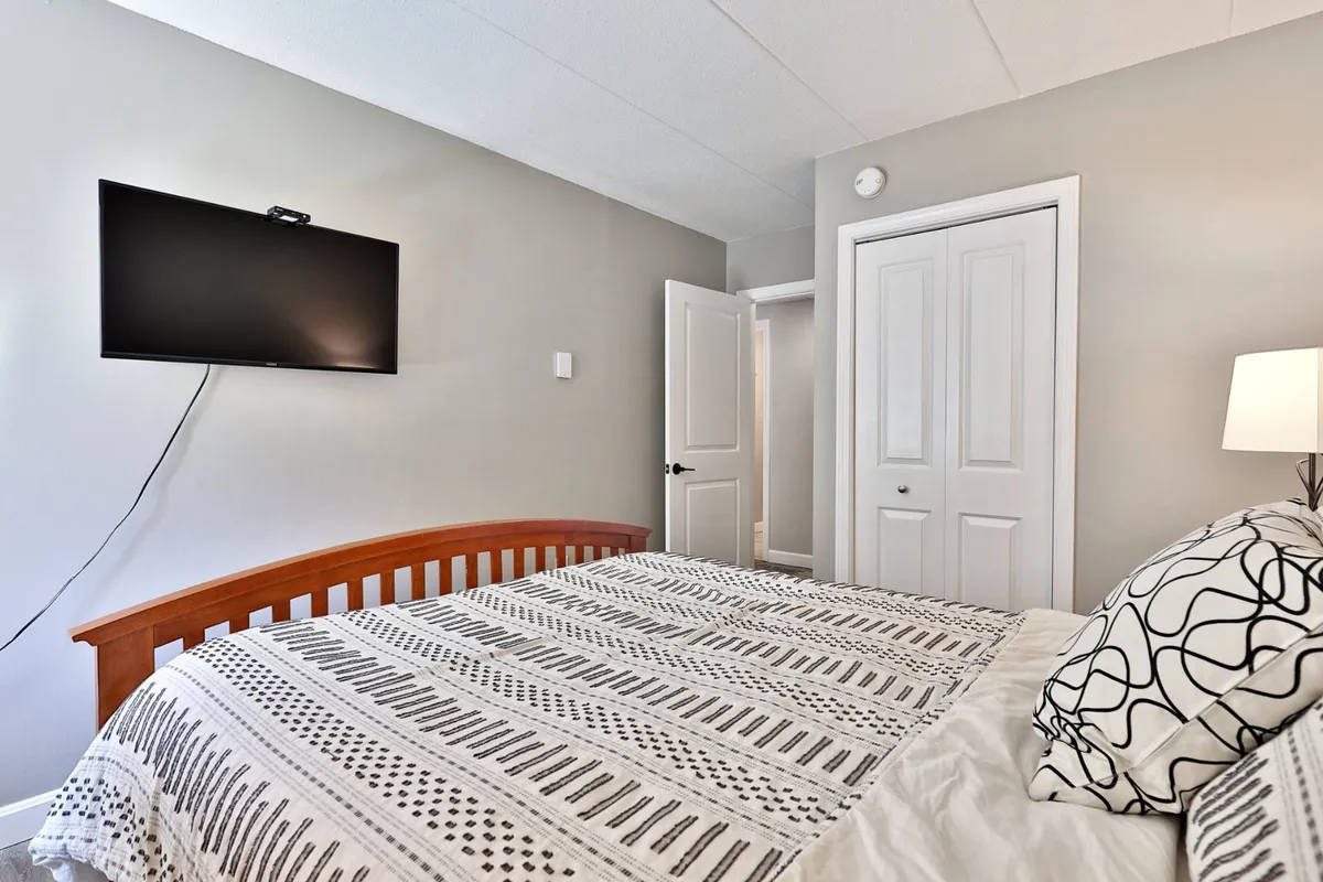 A cozy bedroom with a bed dressed in patterned bedding, a wall-mounted flat-screen TV, and a door leading to another room. The space feels inviting and comfortable, ideal for restful nights or cozy movie sessions.