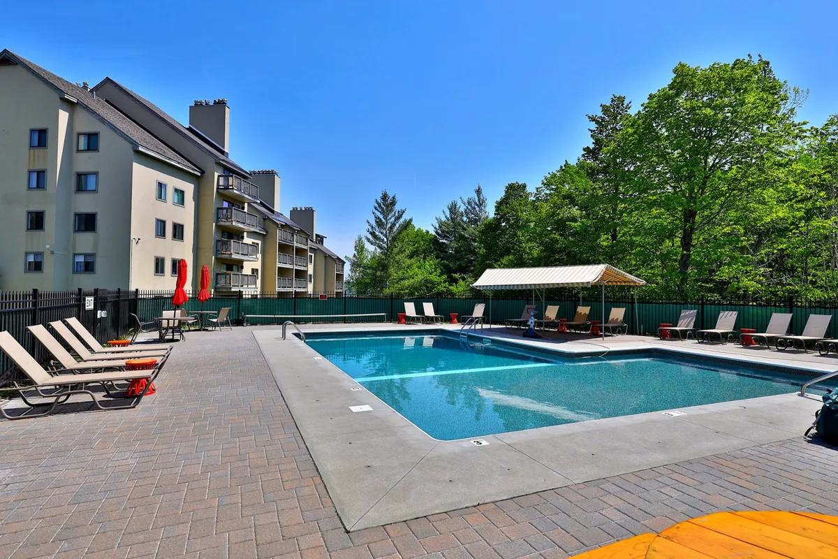 An inviting exterior view of a sparkling swimming pool, poolside loungers, green trees, and a cabana. The atmosphere is relaxed and refreshing, embodying the idyllic summer day experience. The setting is ideal for both adults and kids to enjoy swimming, sunbathing, or community events like BBQs.