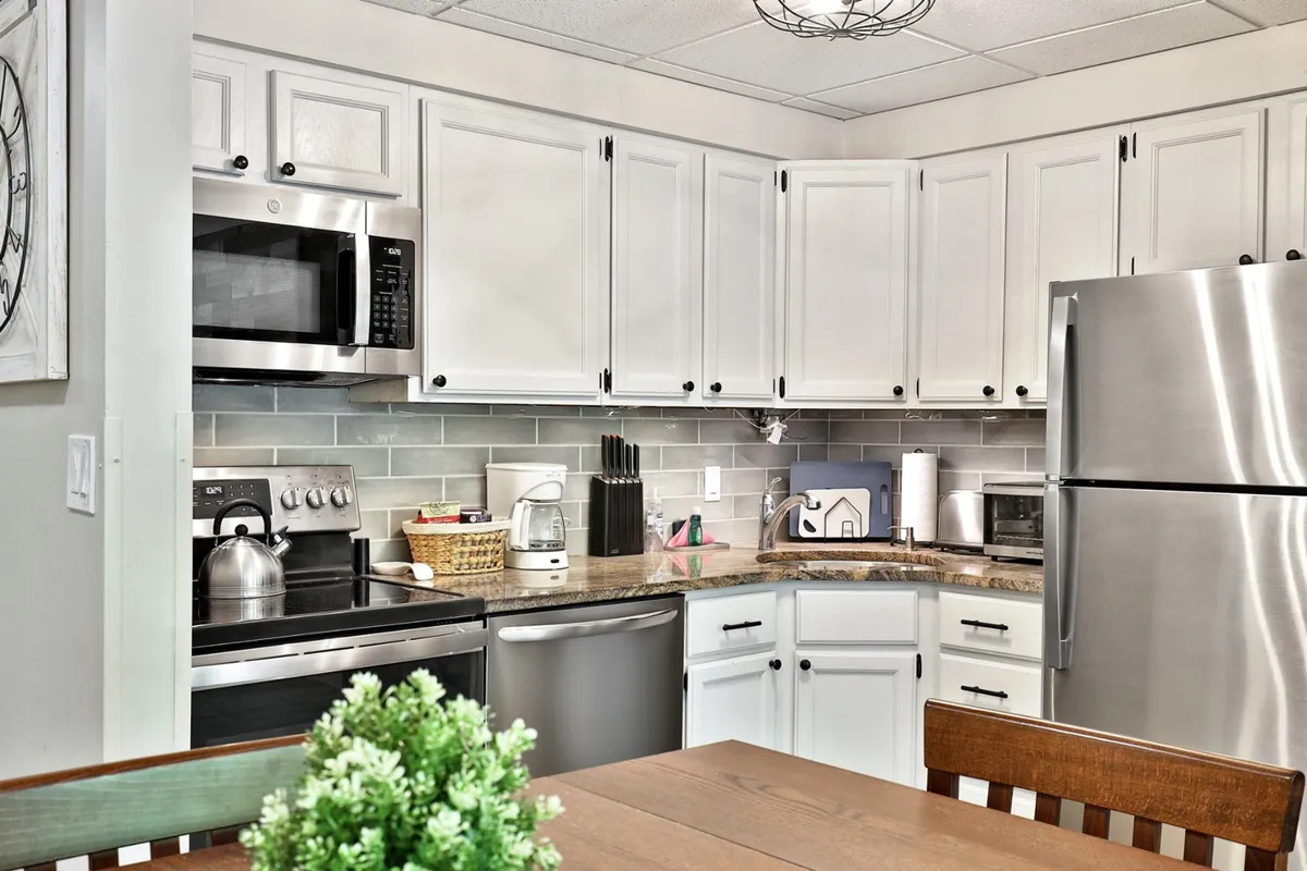 A cozy kitchen scene with modern appliances, a granite countertop, a dining table in the foreground, and a decorative plant adding a touch of freshness. The kitchen is open to the dining area, making it easy for the chef to engage with guests.