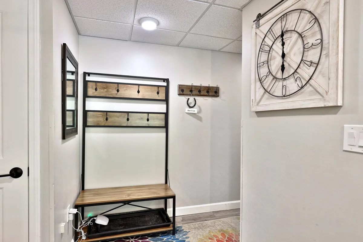 The entry zone with a coat rack ready for winter gear, a wall clock, and a vibrant rug. This area feels prepared for families and groups returning from outdoor activities, emphasizing order and readiness.