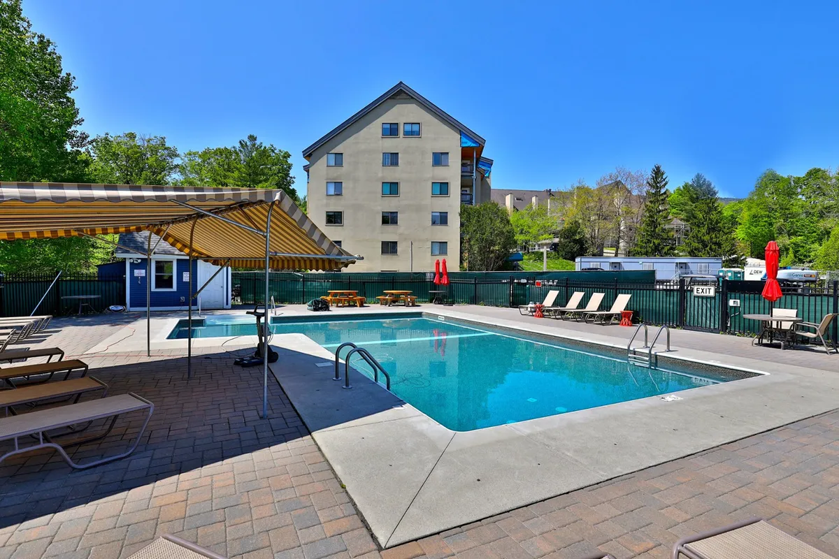 A view of the resort's swimming pool surrounded by lounge chairs and landscaping, with the soft glow of sunset creating a leisurely, sociable atmosphere. The scene suggests daytime relaxation or a casual spot for afternoon socializing before heading out on the town.