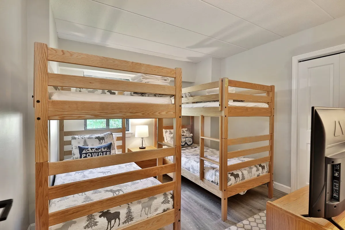 A family-friendly bedroom with two bunk beds, each adorned with decorative pillows. A small lamp and a TV are also visible, creating a cheerful and playful space for kids or friends.